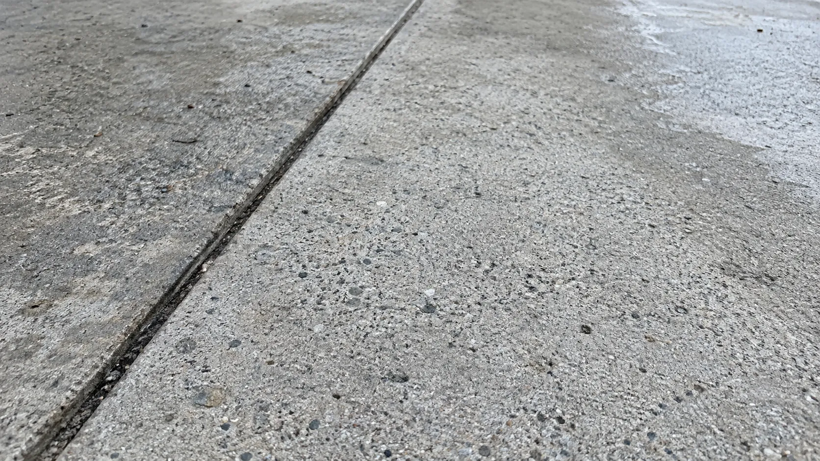 Damp gray driveway concrete with a diagonal expansion joint and natural aggregate texture